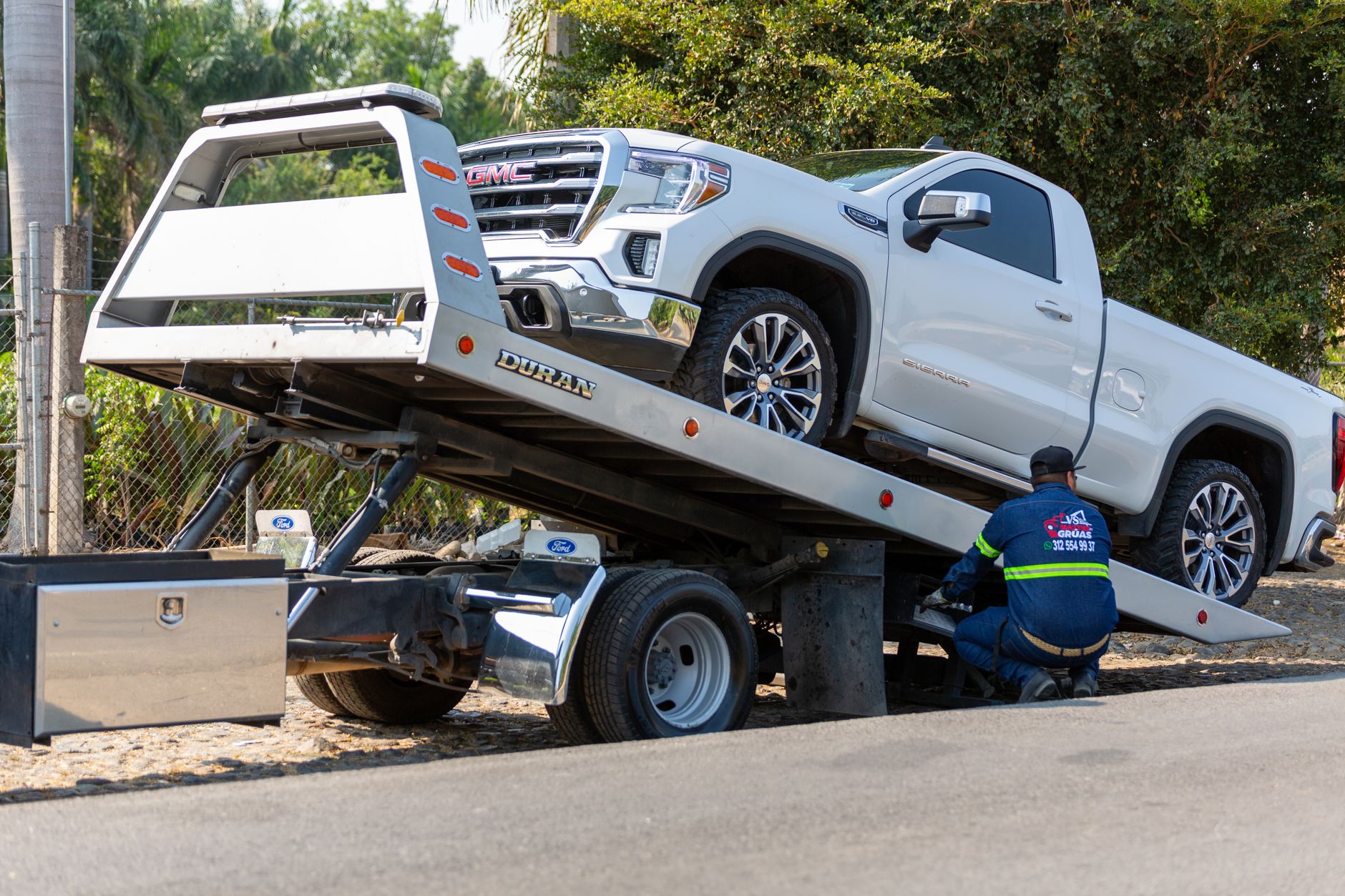 Tow truck operator loading white pickup truck
