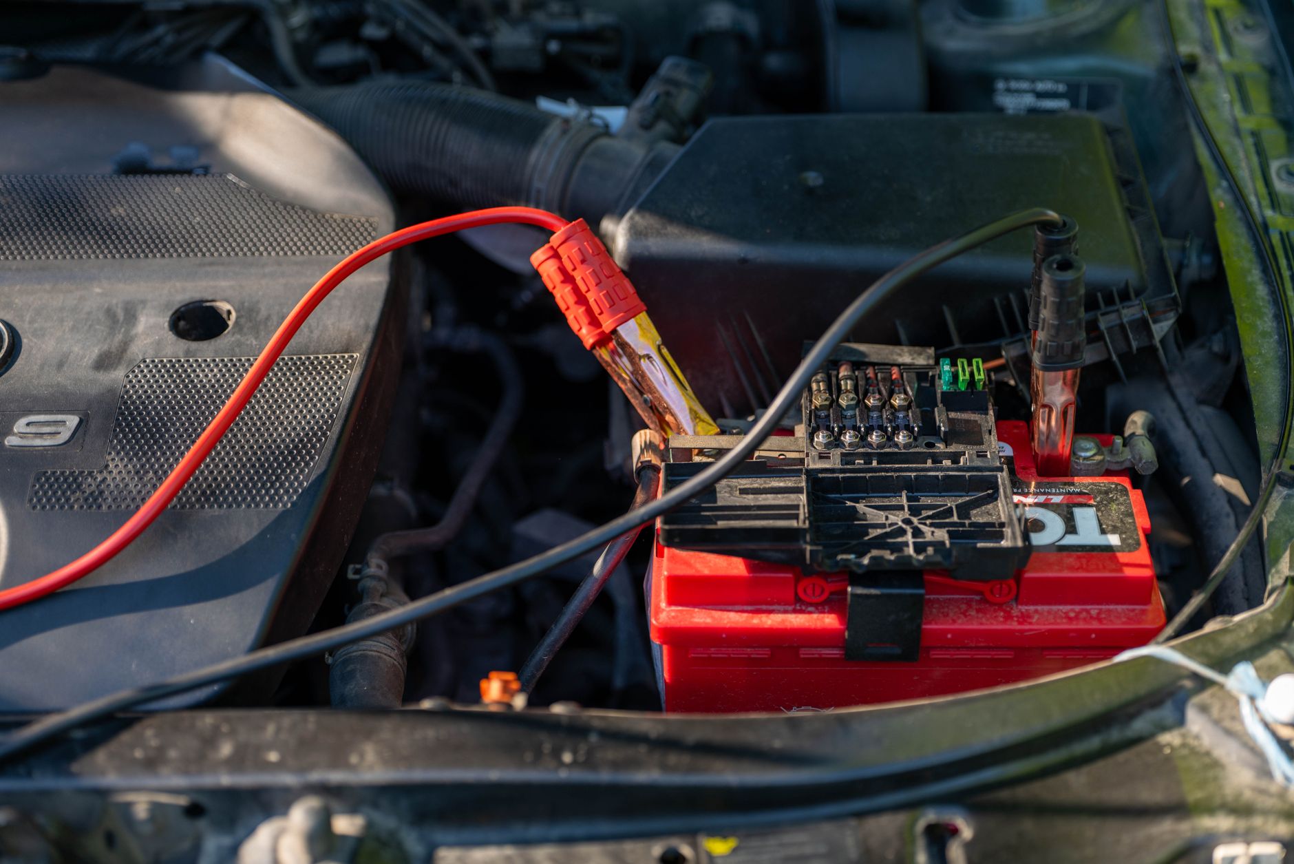 Close-up of a car battery with attached jumper cables in an engine bay