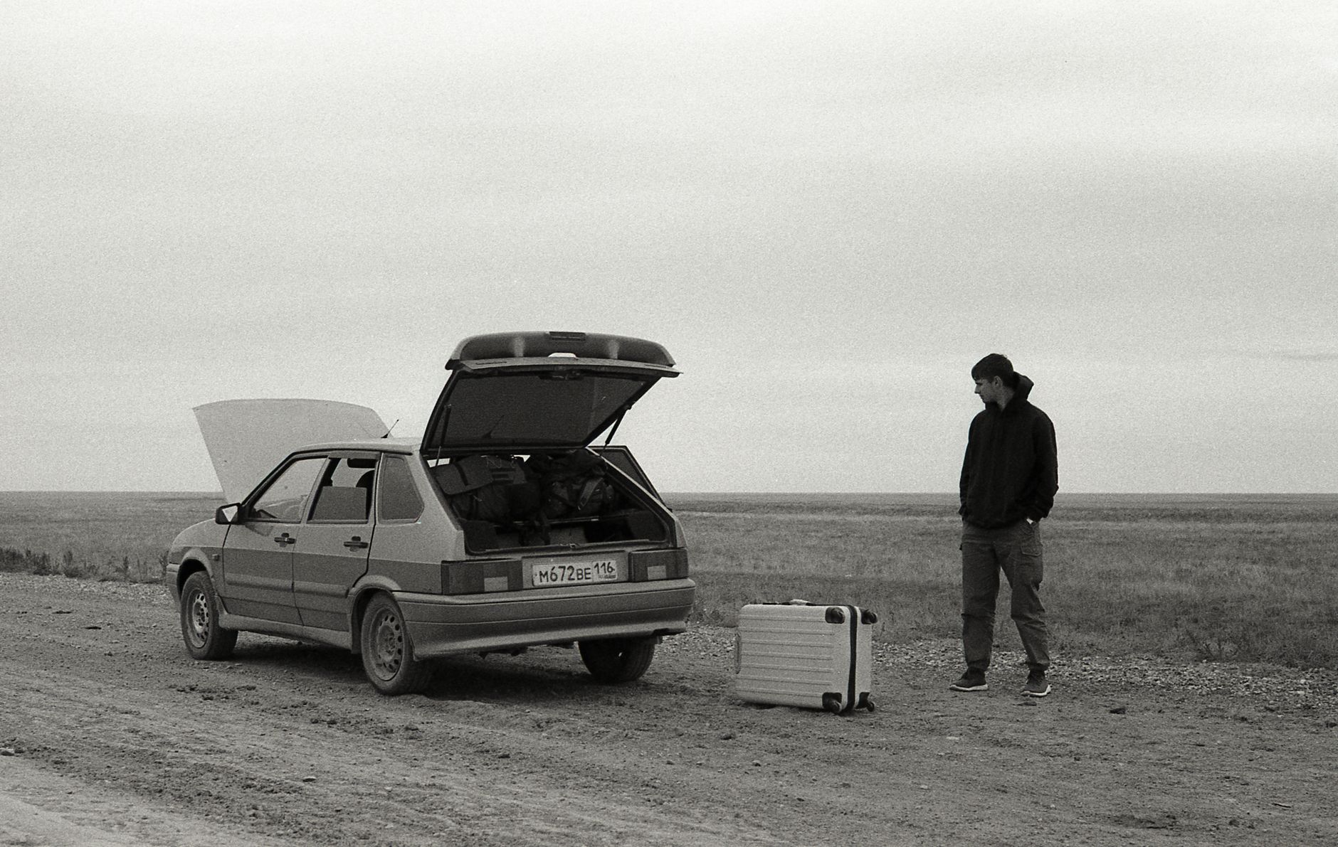Person waiting by a broken down car on a rural road