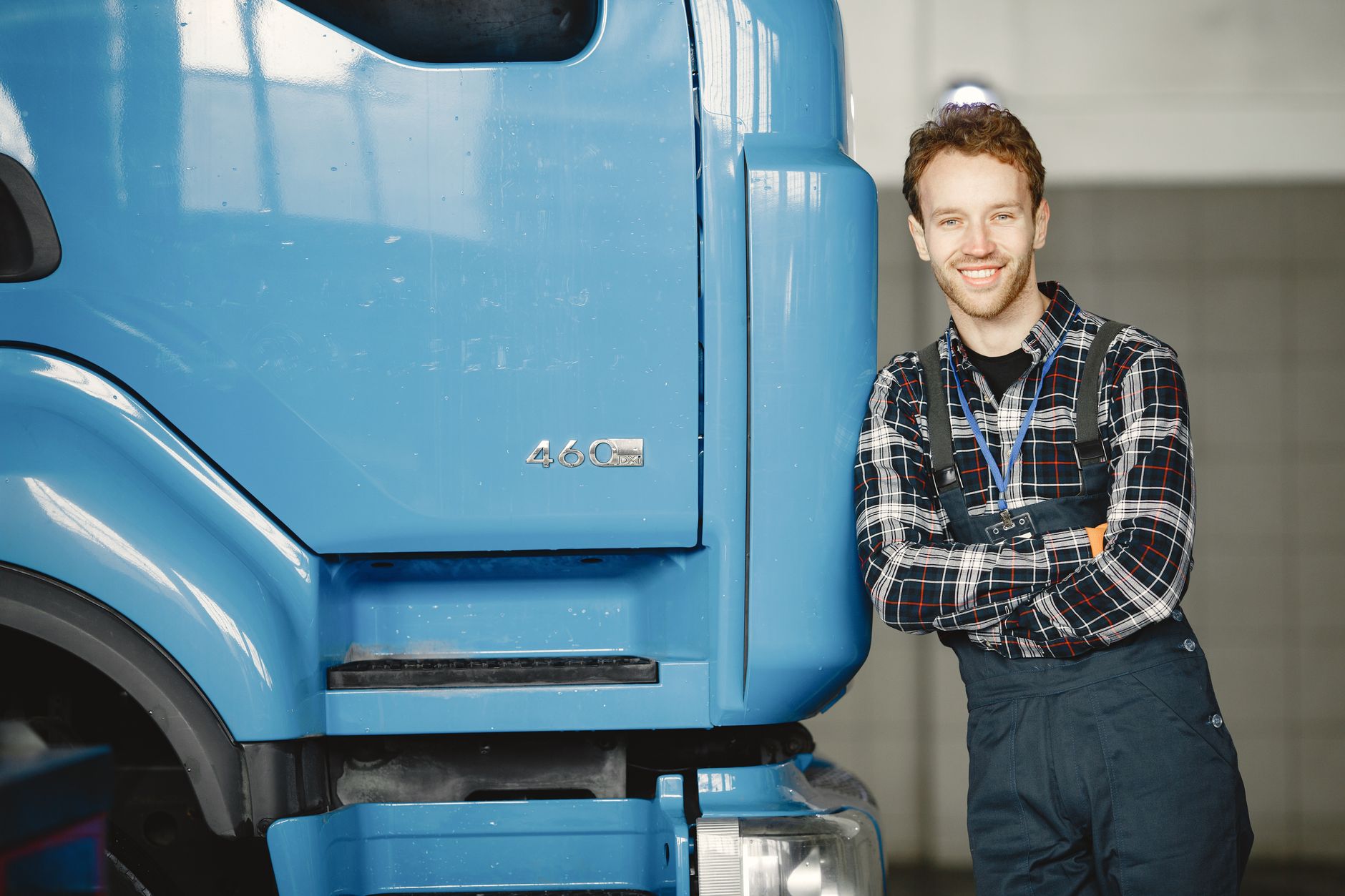 Friendly auto mechanic leaning on a blue truck, smiling