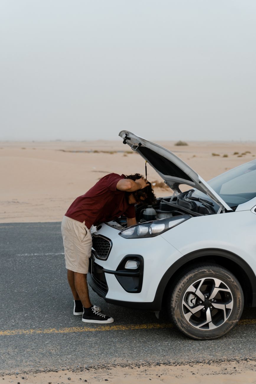 A man checks under the hood of a broken car on a deserted road