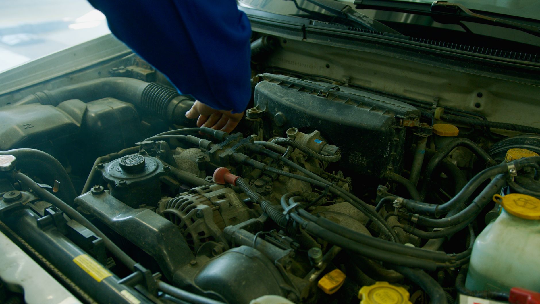 Mechanic in blue uniform working on a car engine in a garage environment