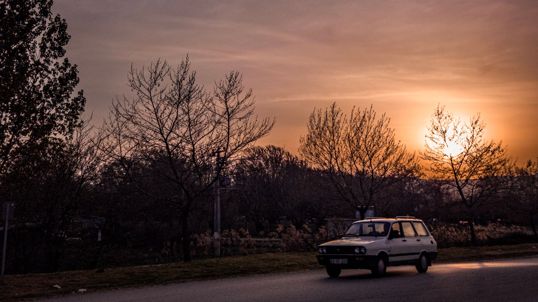 A vintage car traveling on a scenic road during a beautiful sunset