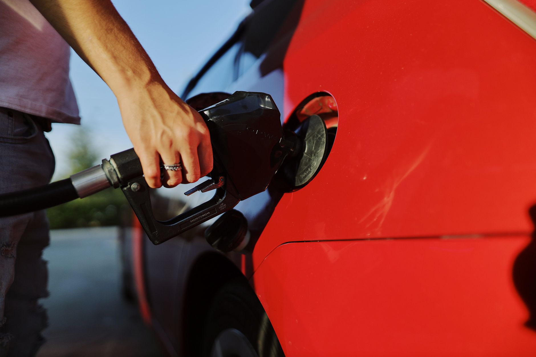 Person pouring gasoline from a red jerry can into a car tank