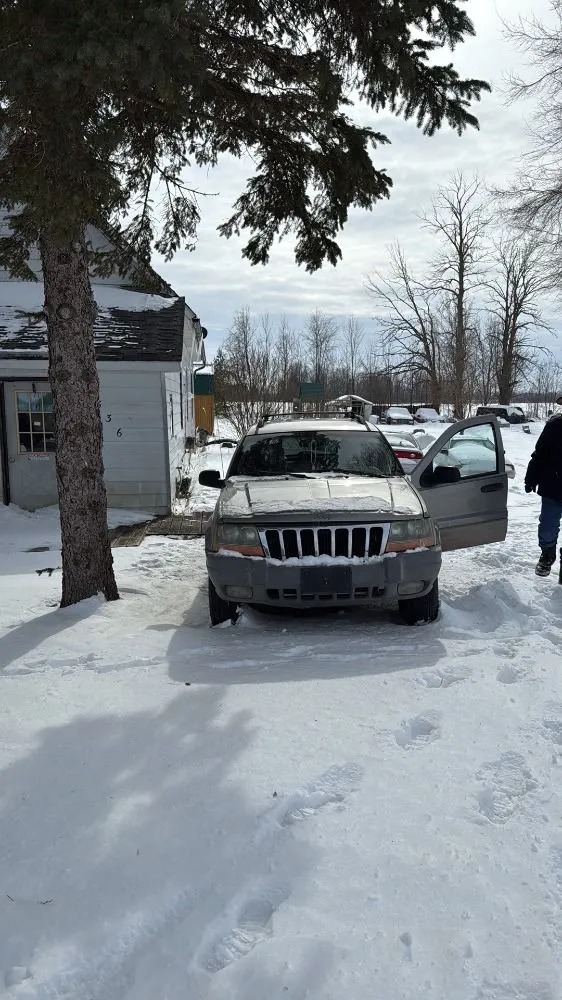 A gold SUV parked in a snowy yard next to a white building, with a person standing by the open driver-side door.