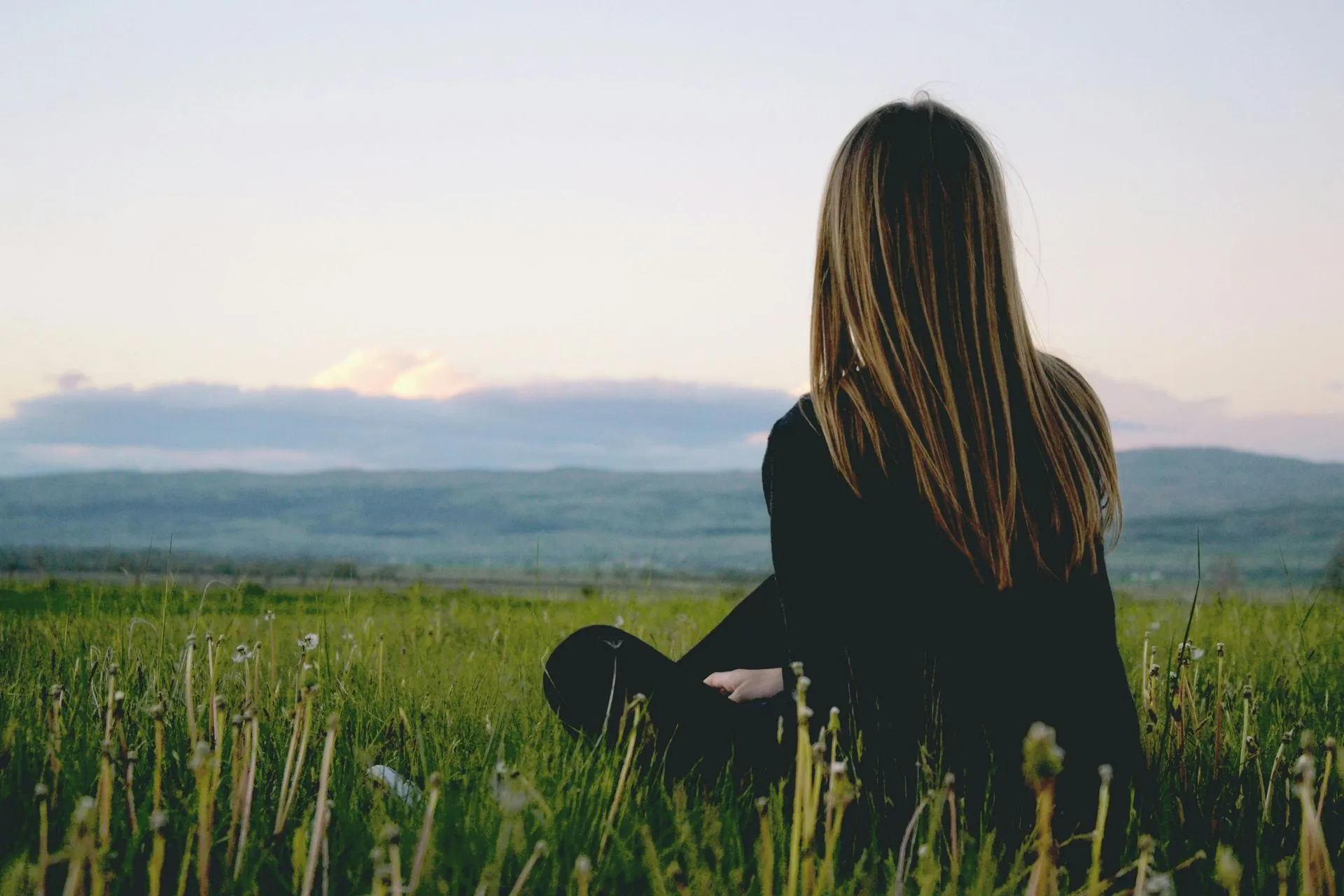 A woman is sitting in the grass looking at the mountains