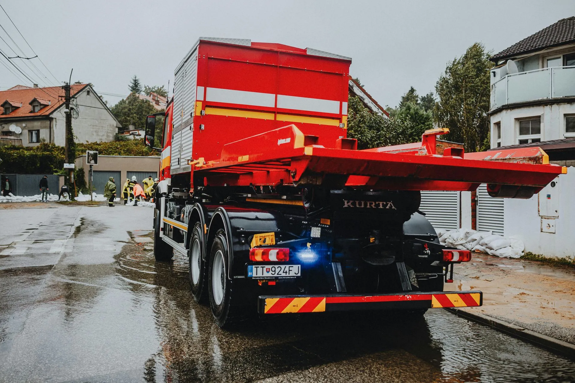 A red and white truck is driving down a wet street