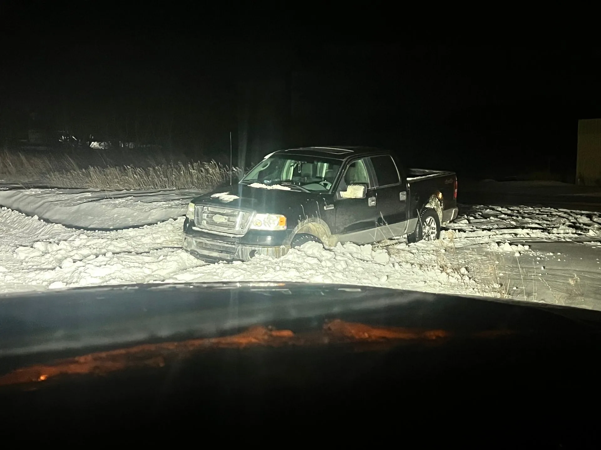 A black truck is stuck in the snow at night