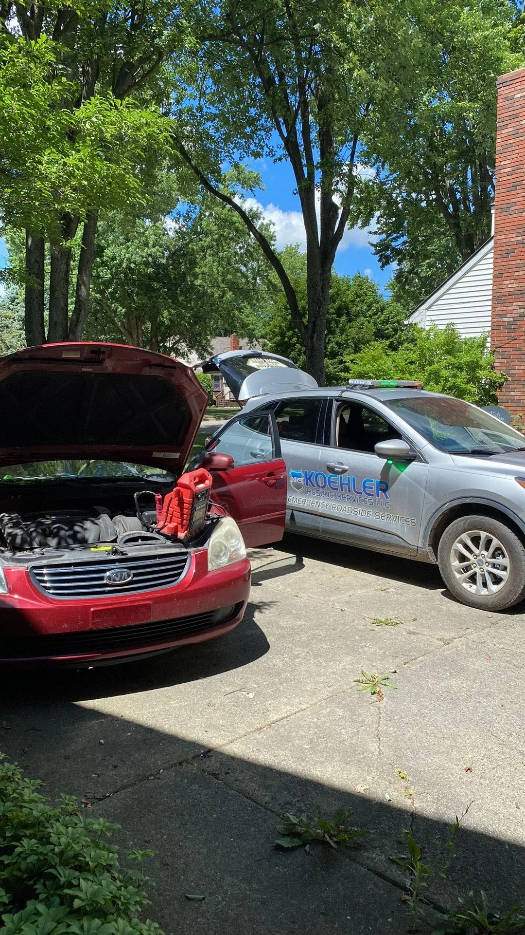 A red car is parked next to a silver car with its hood open.