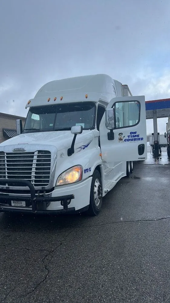 A white semi truck is parked in front of a gas station with its doors open.