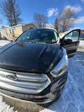 A black ford escape is parked in the snow with its doors open