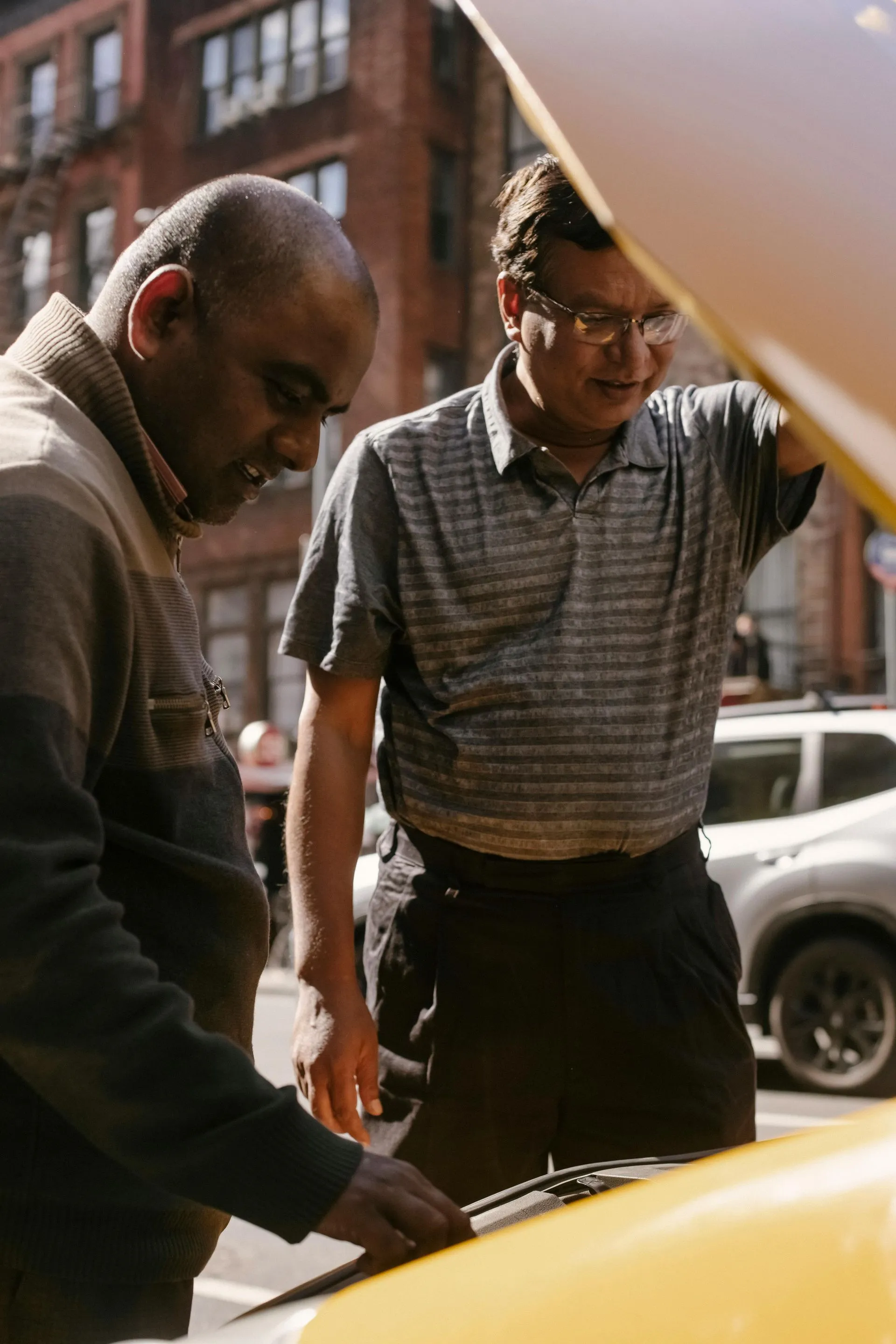 Two men are looking under the hood of a yellow car