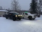 Two trucks are parked in the snow in front of a house