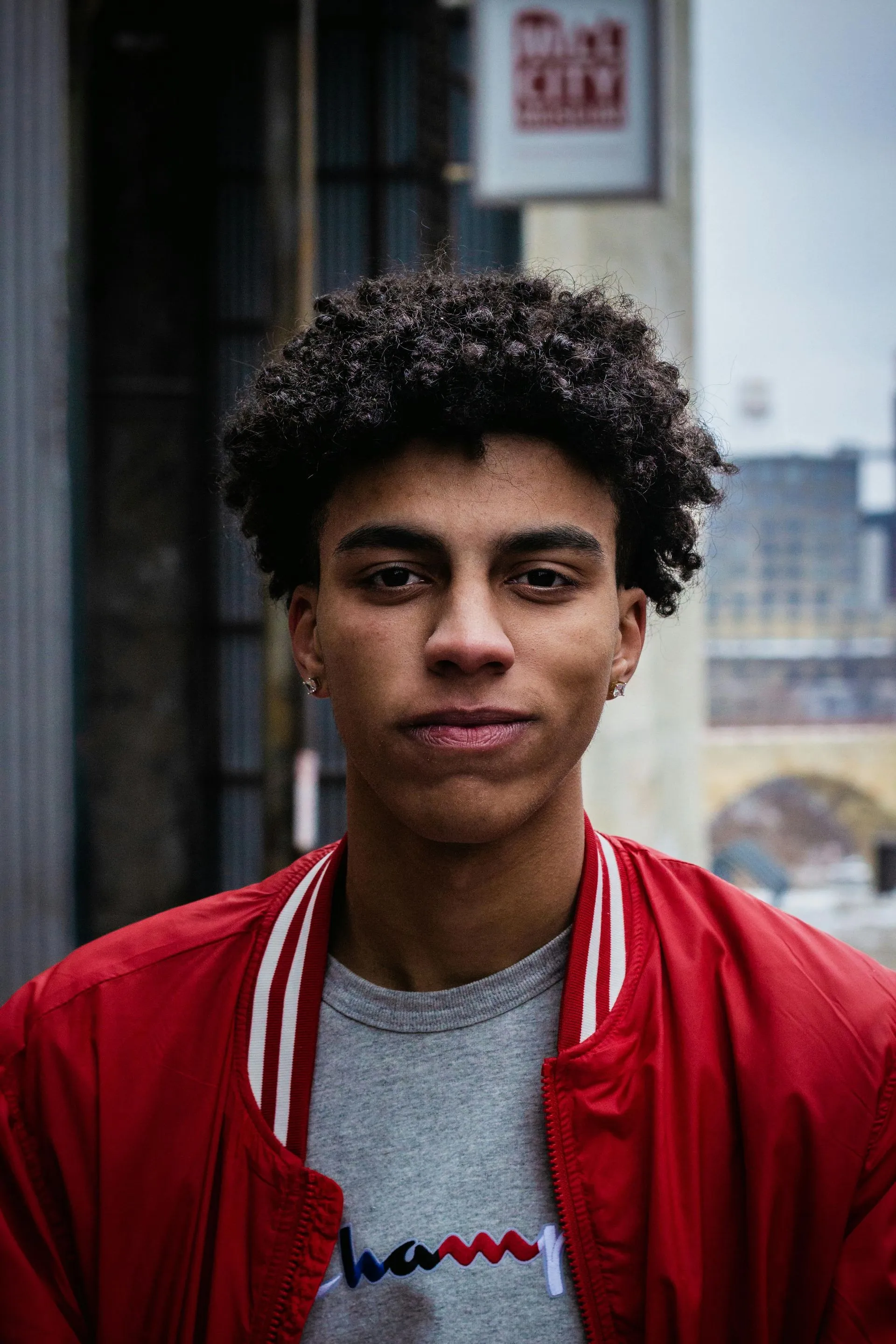 A young man with curly hair is wearing a red jacket and a gray t-shirt